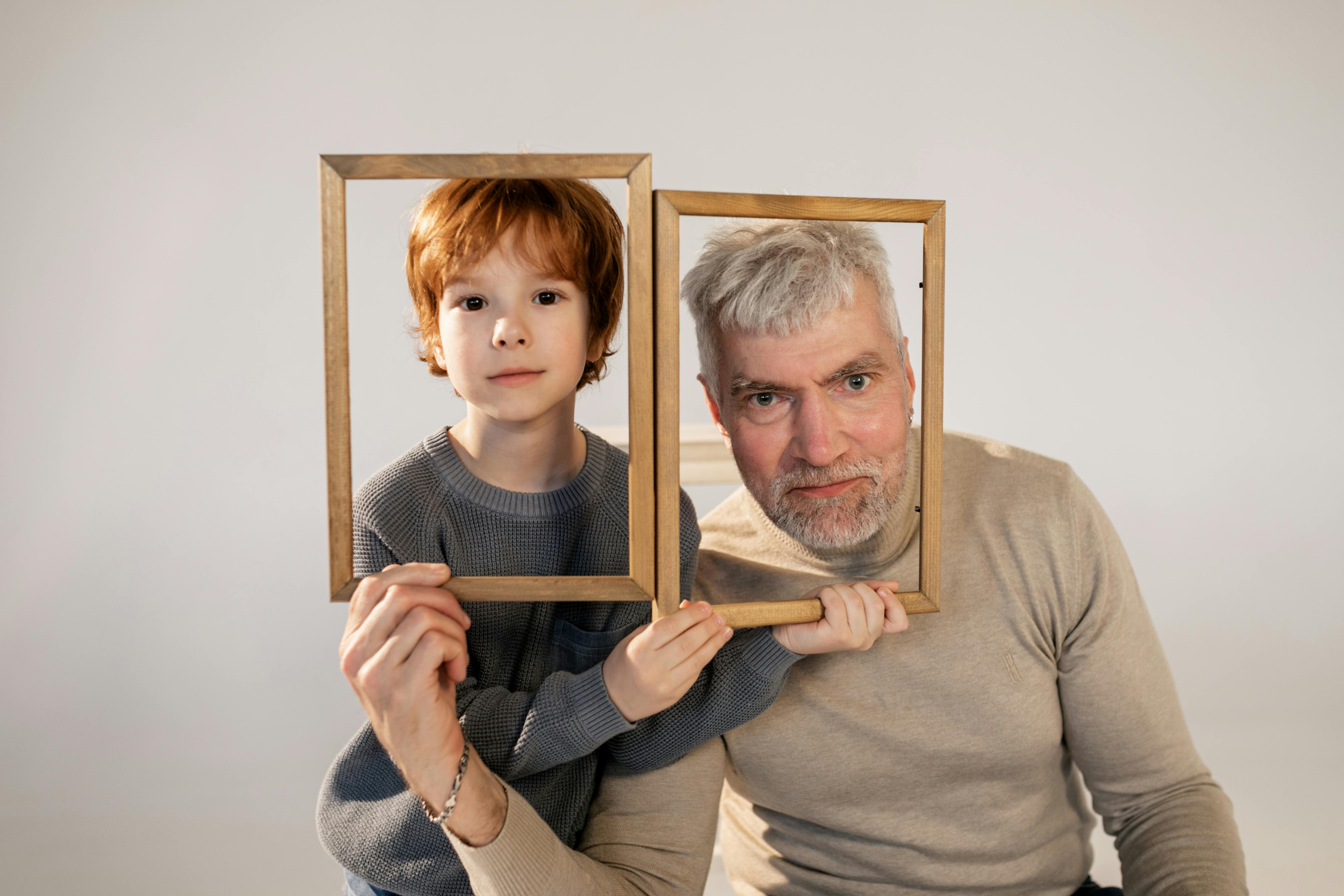 Free A touching portrait of a grandfather and grandson holding wooden frames, symbolizing family bonds. Stock Photo