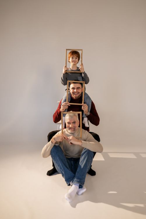 Free Three generations sit in a creative family portrait holding picture frames, smiling in a studio setting. Stock Photo