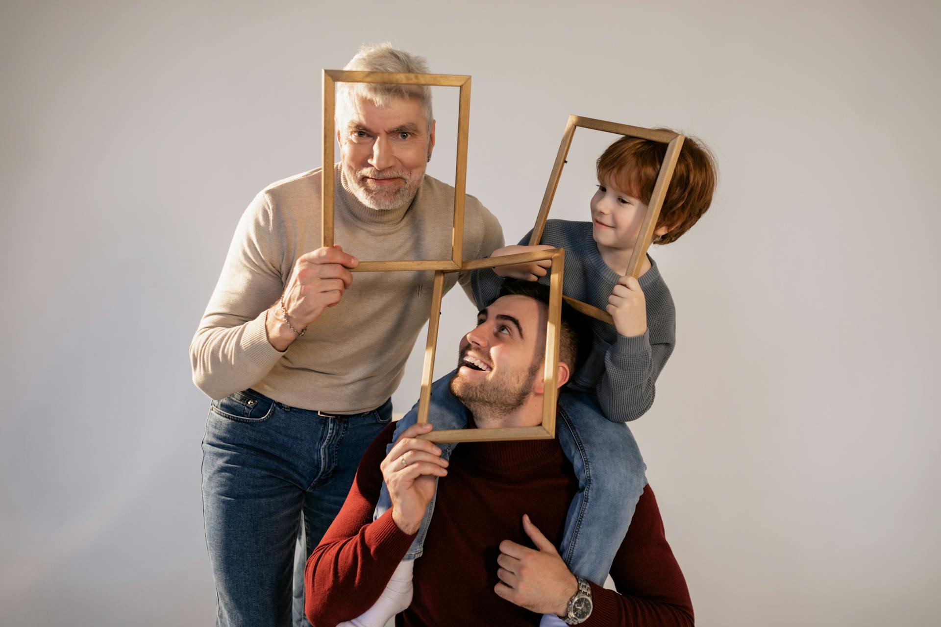 Playful family portrait session with grandfather, father, and son using picture frames.