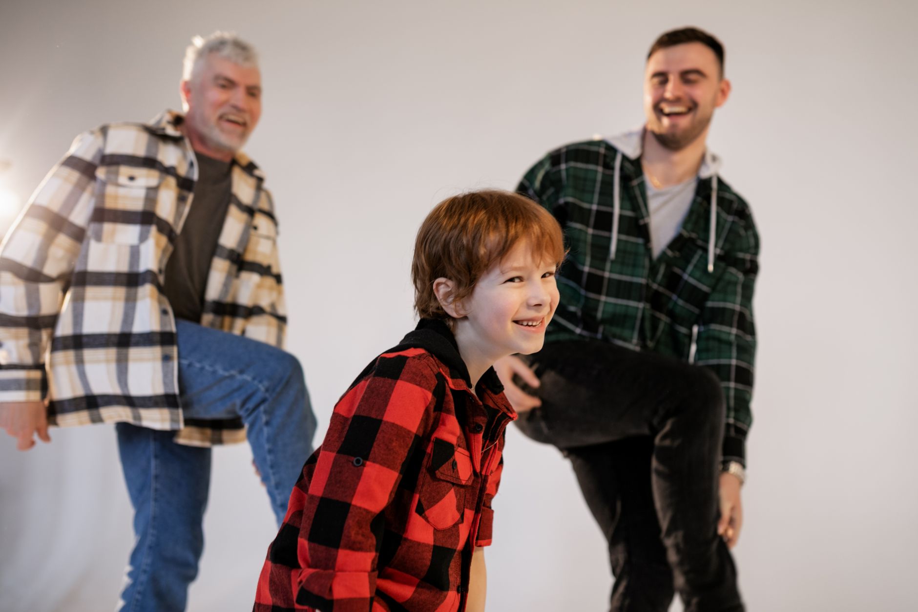 A joyful moment shared among three generations wearing plaid shirts, smiling and having fun indoors.