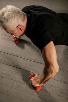 A senior man performing push-ups with red dumbbells indoors, focusing on strength and fitness.