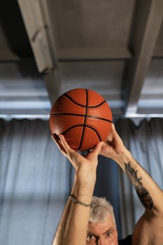 Senior man with tattoo shooting basketball indoors, emphasizing active lifestyle.