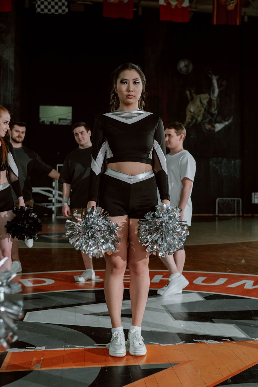 A diverse cheerleading team in uniform performing indoors with pompoms.