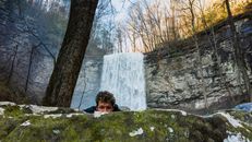 Young male hiker hiding behind boulder near waterfall in forest