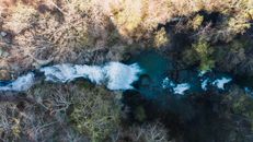 Spectacular drone view of rapid waterfall flowing amidst leafless autumn trees through rocky cliff in Cloudland Canyon on sunny day