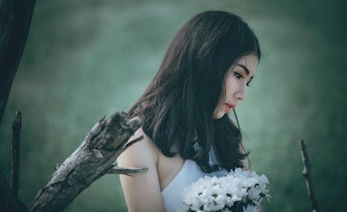 Frau In Der Weißen Spitze, Die Blumenstrauß Der Weißen Blütenblätter Hält, Während Sie Nach Unten Schaut
