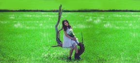 一位年轻女子身穿白色连衣裙，手捧花束，站在郁郁葱葱的绿色田野上，尽显自然之美