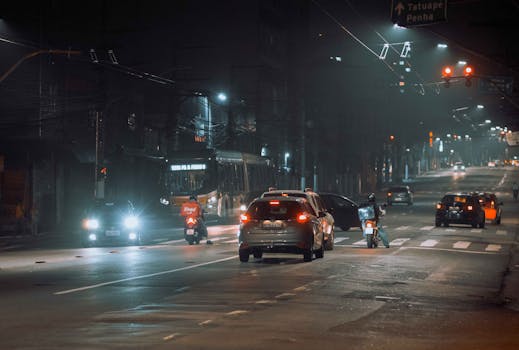 A busy city street at night featuring cars, a bus, and a motorbike under streetlights.