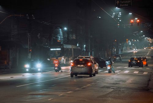 Free A busy city street at night featuring cars, a bus, and a motorbike under streetlights. Stock Photo