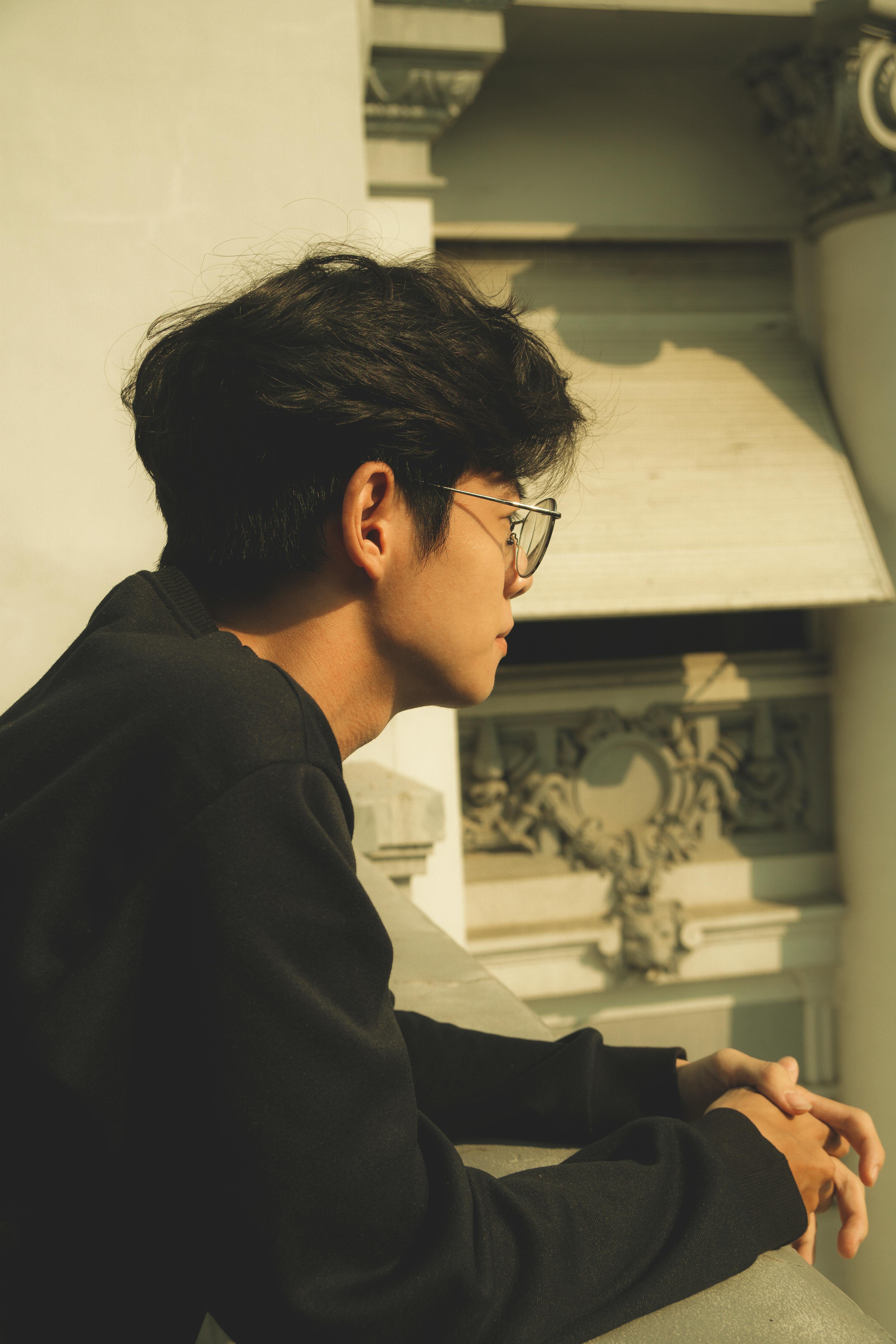 Young man with glasses leaning on a railing in Vietnam, gazing pensively outdoors.