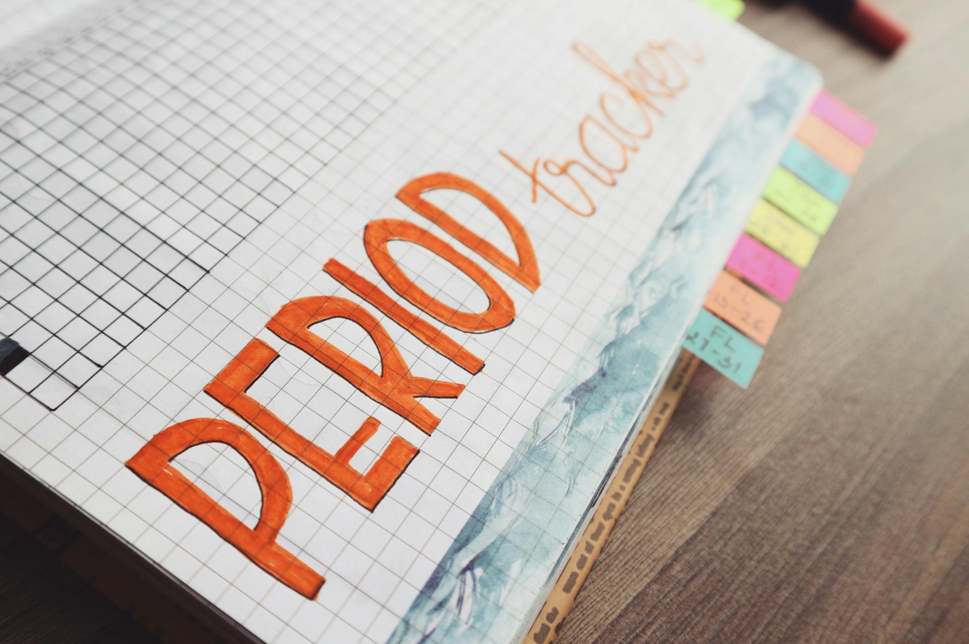 Close-up of a handwritten period tracker in a grid-lined journal on a wooden table.