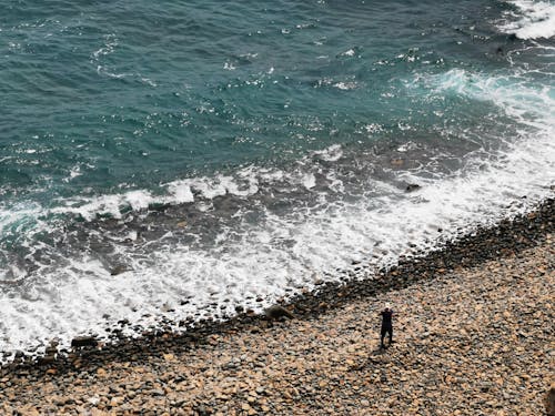 Photo of a Person Standing on a Rocky Seashore