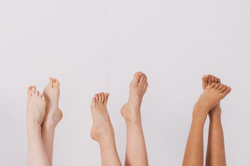 Free Four pairs of diverse feet raised against a plain white backdrop, capturing unity and diversity. Stock Photo