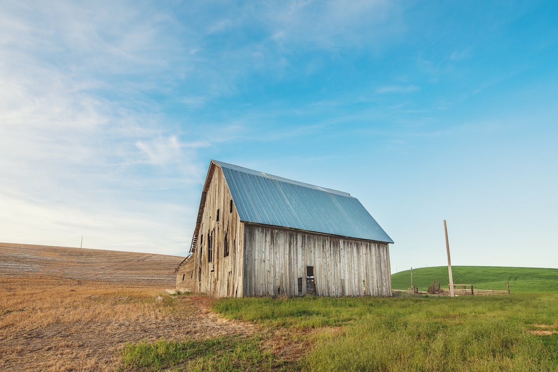 米色和灰色木製穀倉房子在綠色草地上的照片
