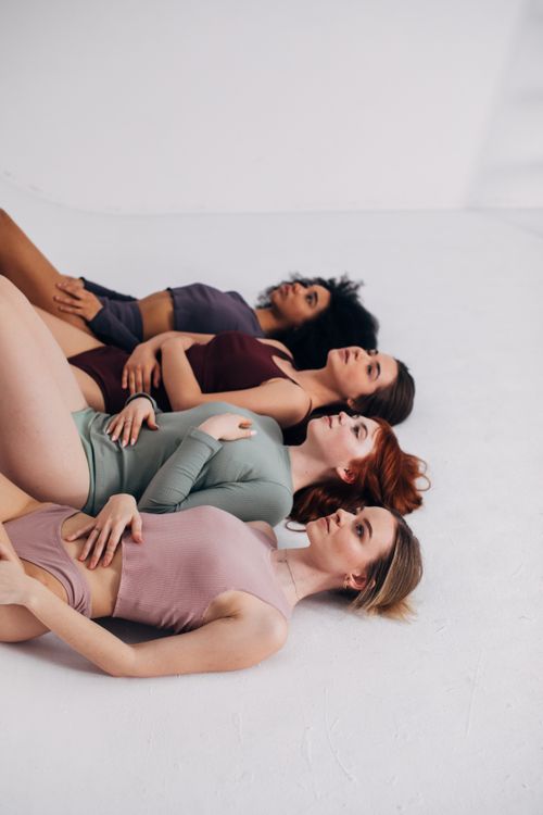Free Four diverse women lying on the floor in pastel outfits, promoting empowerment. Stock Photo