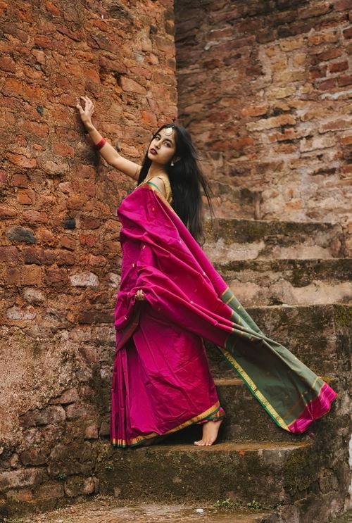 Free A woman in a vibrant saree poses against a rustic brick wall, exuding grace and style. Stock Photo