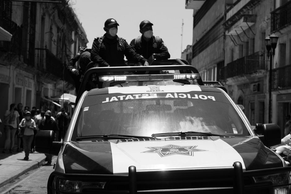 workers sitting in the back of a pickup truck or van, looking worried, with law enforcement nearby