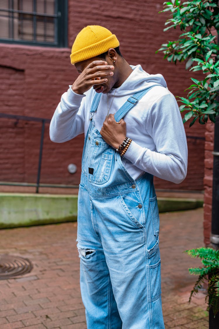 A Man In Overalls Rubbing His Eye