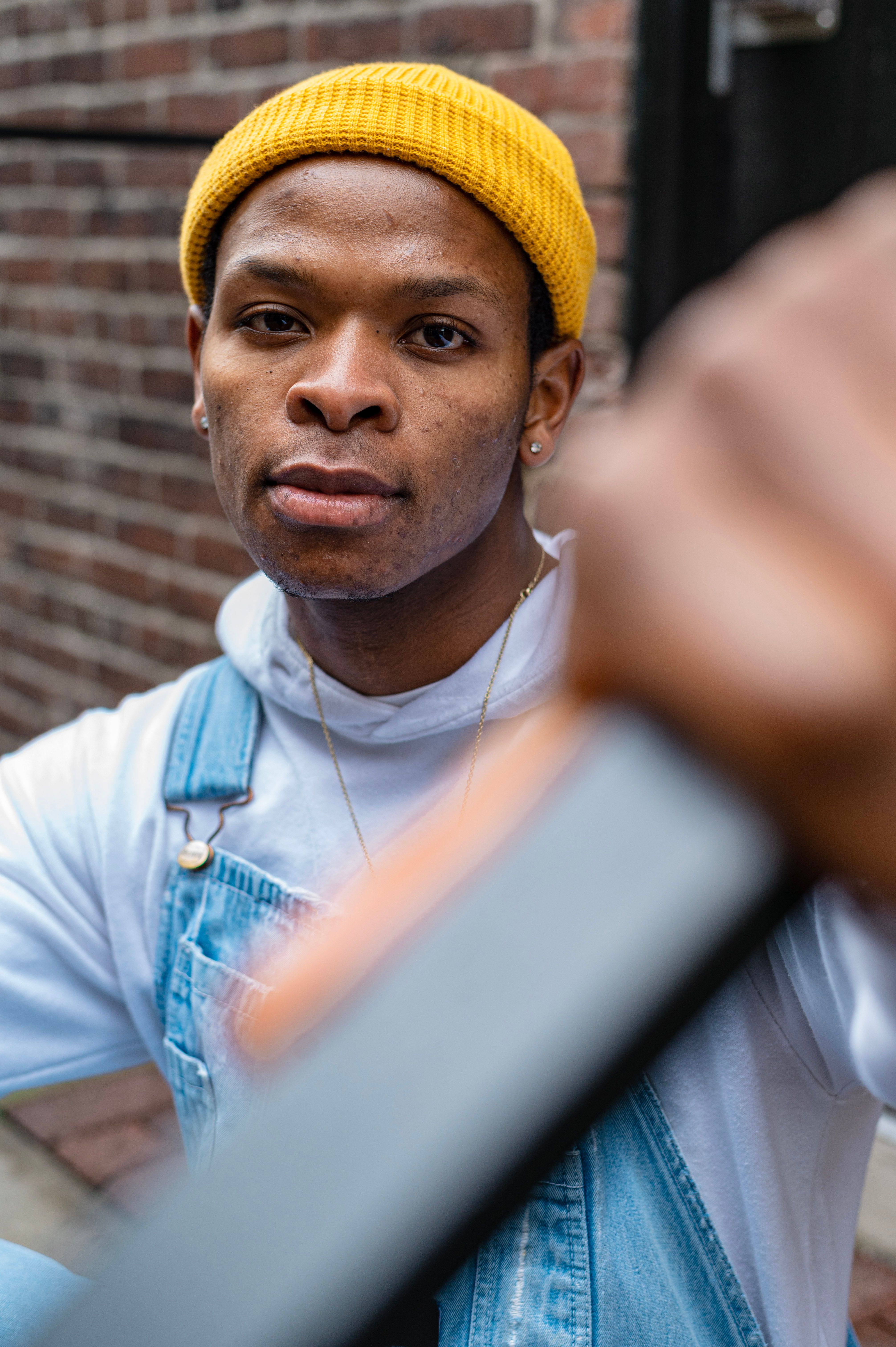 Stylish young man in a yellow beanie and overalls posing outdoors. Urban fashion shoot.