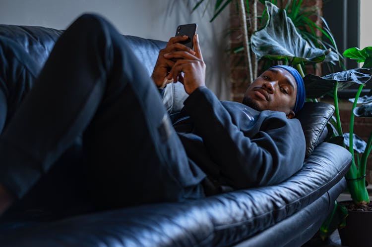 A Man Lying On A Sofa Holding A Cell Phone