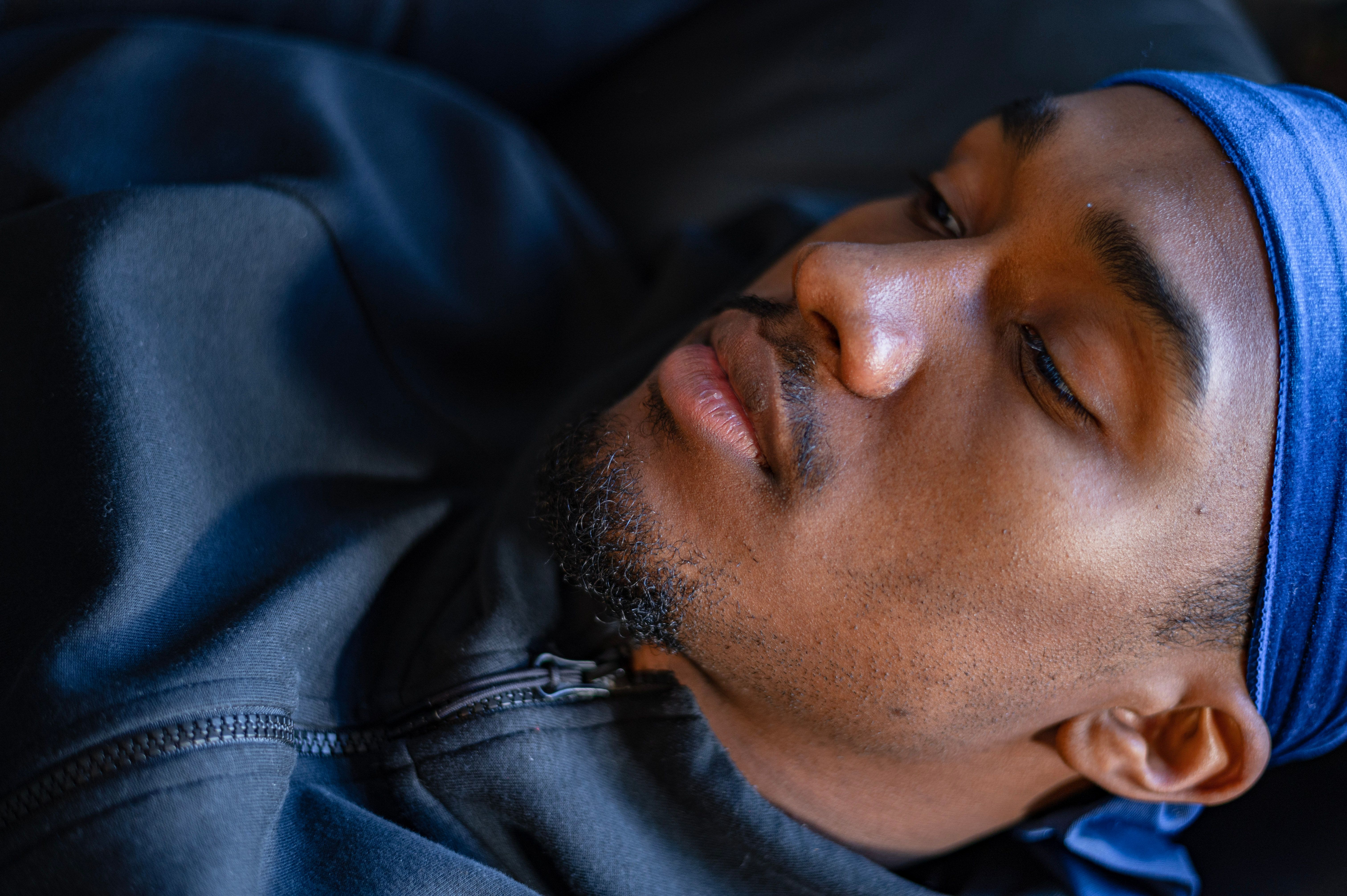 Close-up portrait of a man resting with a calm expression wearing a blue bandana.
