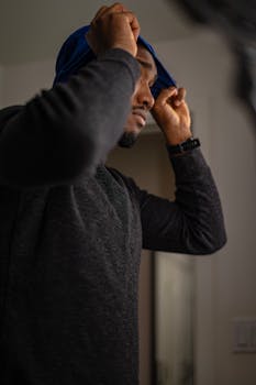 African American man in a cozy sweater adjusts his headwear in a stylish indoor setting.