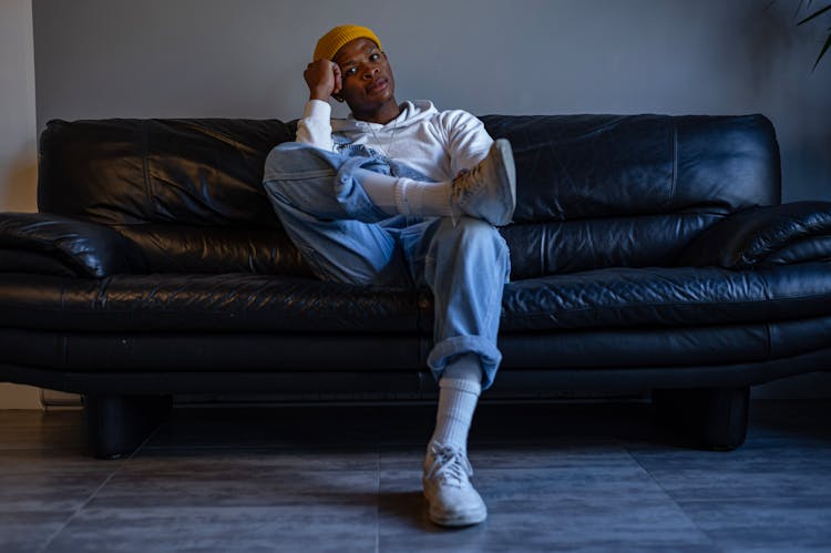 A Man Wearing A Yellow Beanie Hat Sitting On A Sofa 