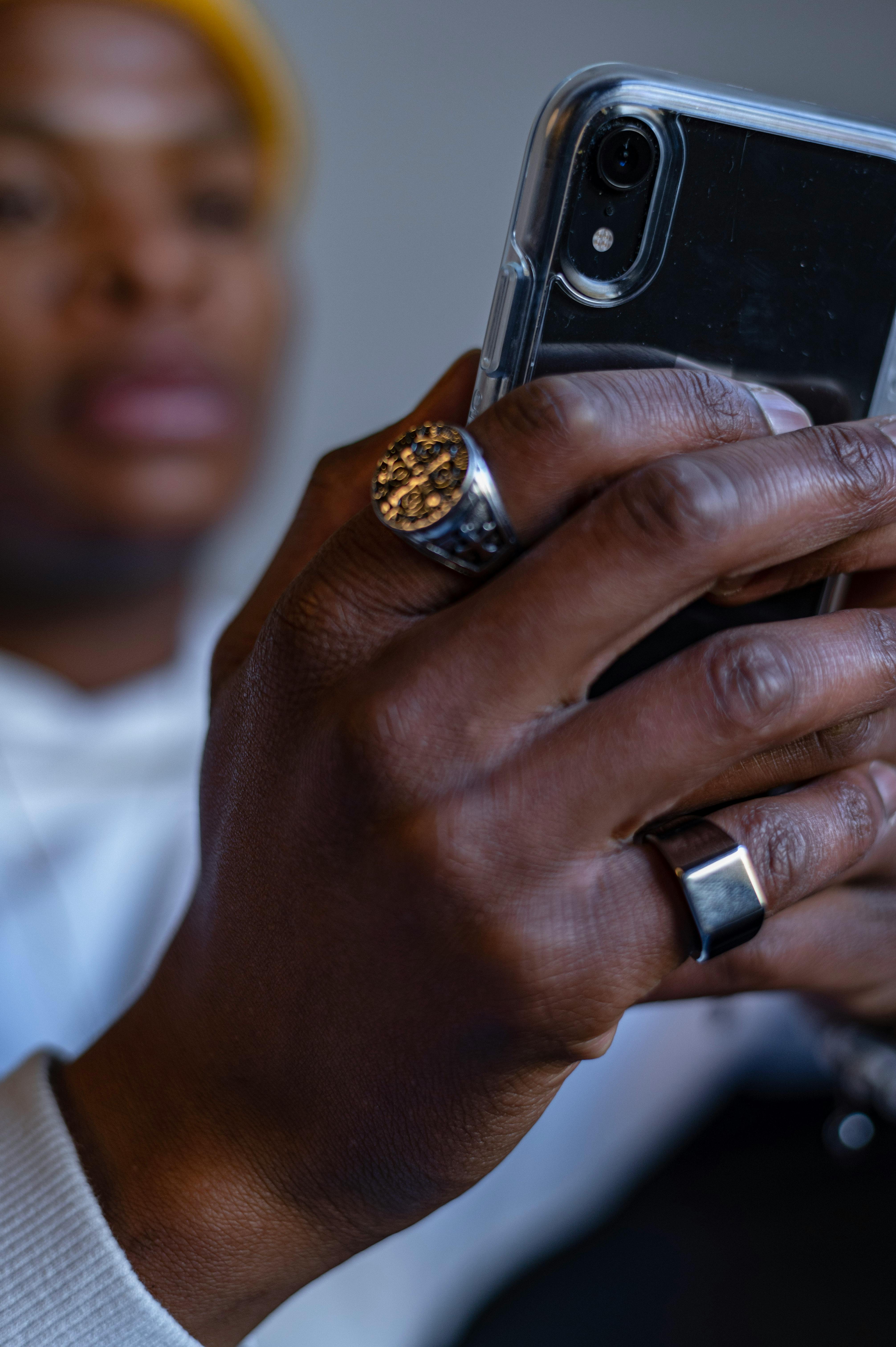 Hand adorned with rings holding a smartphone, showcasing modern style and technology.