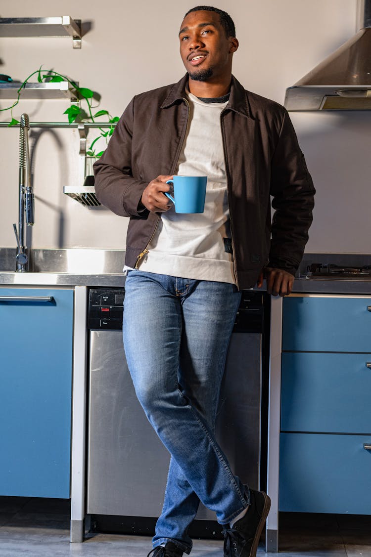 A Man Holding A Mug While Leaning On A Kitchen Counter