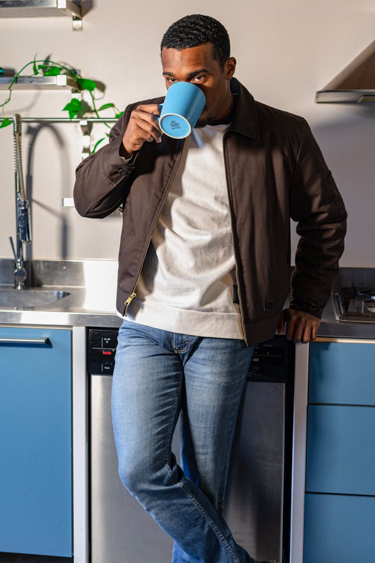 A Man Sipping Coffee While Leaning On A Kitchen Counter