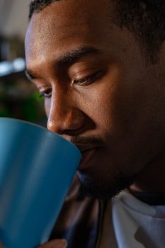 An intimate close-up of a man sipping from a blue mug indoors.