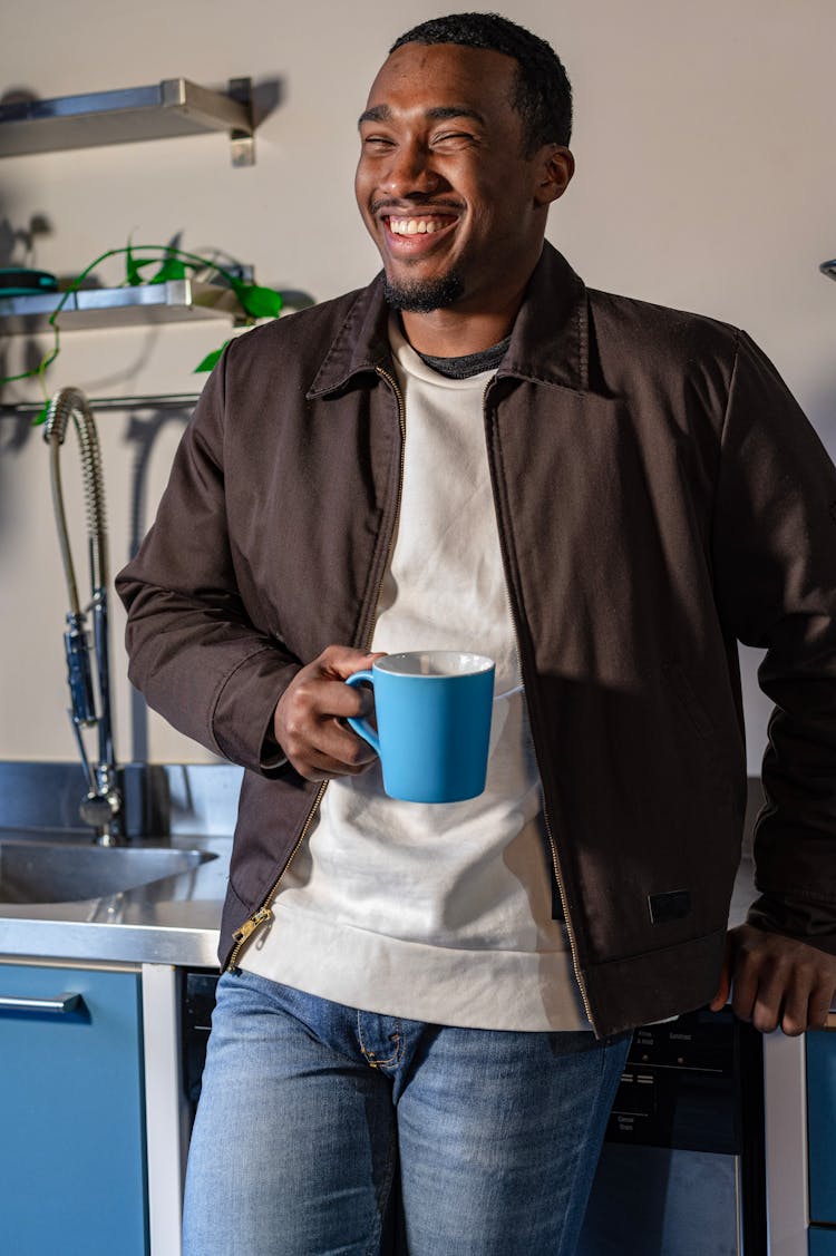 A Happy Man Holding A Mug While Leaning On A Kitchen Counter