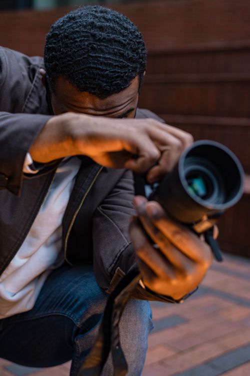 Free Close-up of a young photographer adjusting his DSLR camera outdoors, focusing intently. Stock Photo