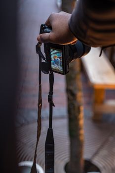 A photographer's hand holds a camera capturing an outdoor scene with a focus on street photography.