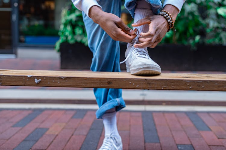 A Person Tying Their Shoe On A Wooden Bench