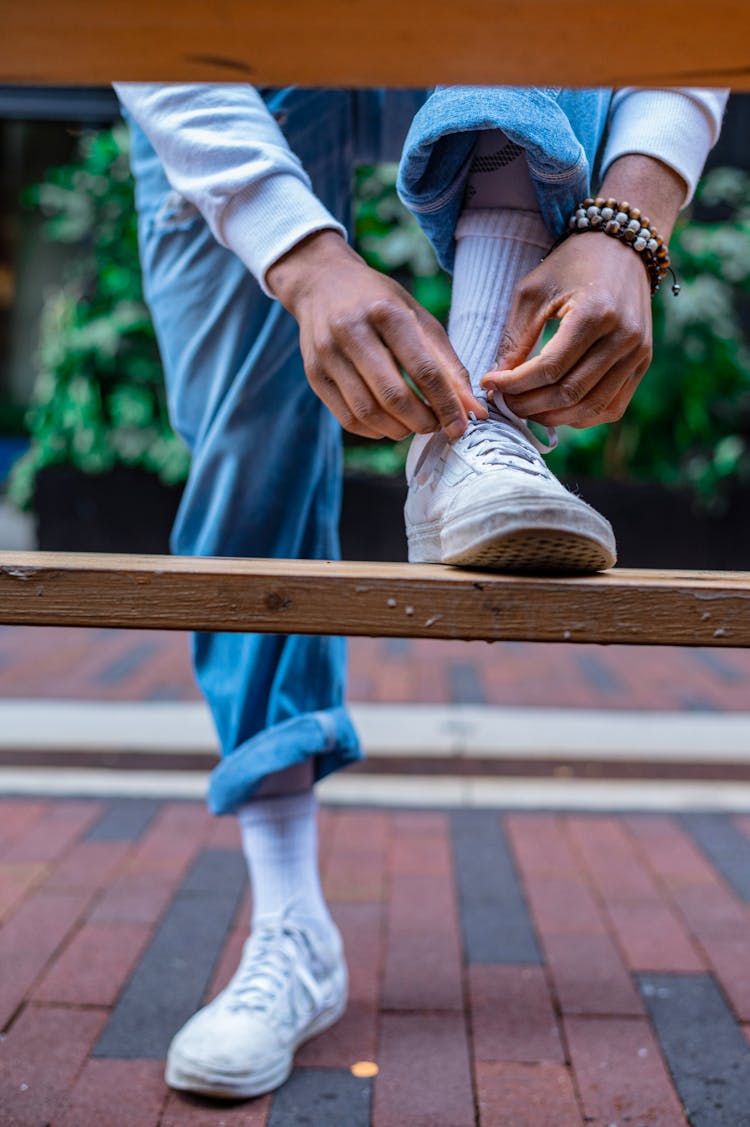 A Person Tying Their Shoe On A Wooden Bench