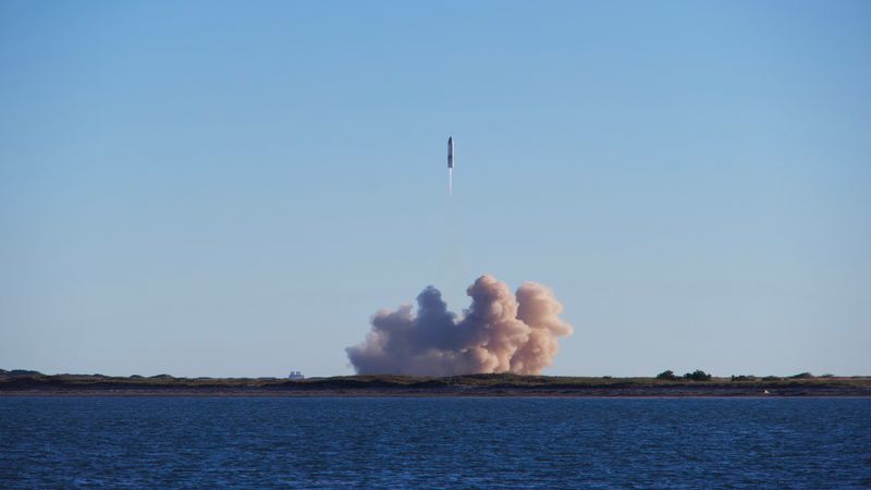 A rocket launch with smoke trails over South Padre Island, viewed across the ocean.