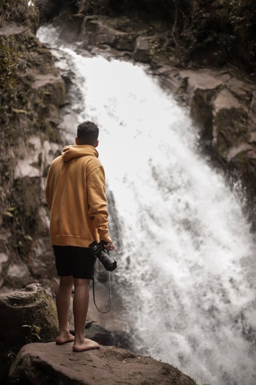 A Photographer Standing on a Rock while Looking at Waterfalls