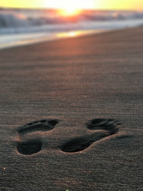 Free Sunset illuminates footprints on Carlsbad Beach, capturing a tranquil moment by the ocean. Stock Photo