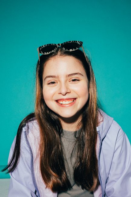Cheerful young girl smiling broadly against a bright turquoise backdrop.