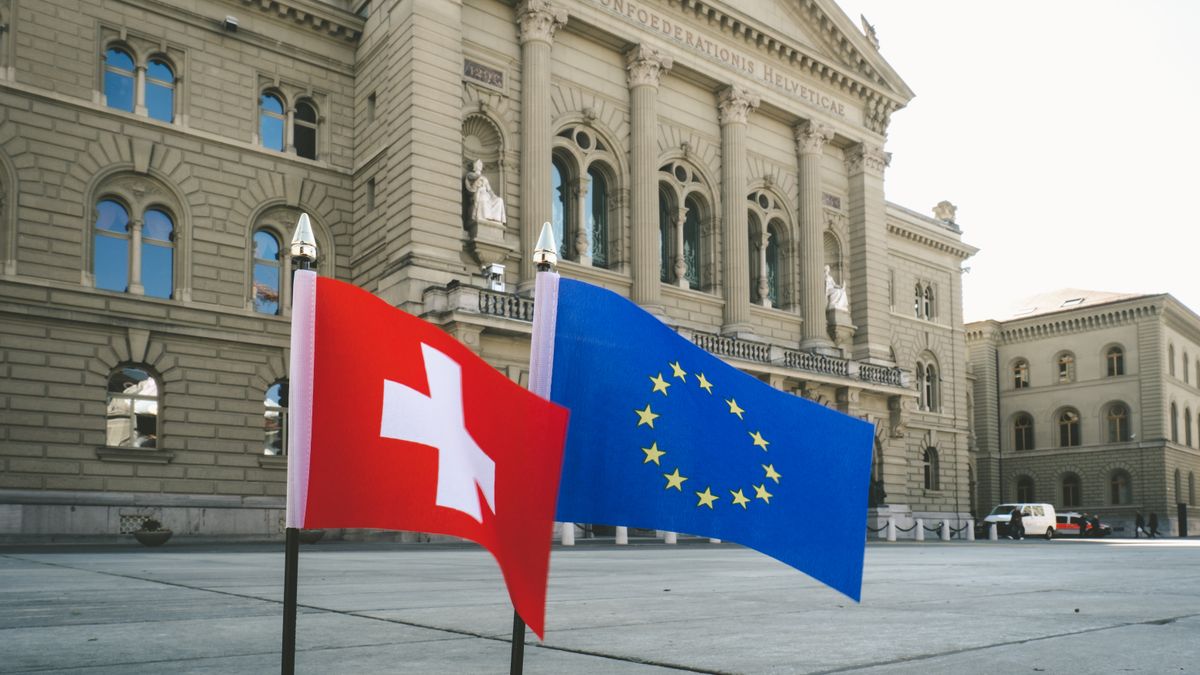 Front view of Swiss Parliament Building in Bern with Swiss and EU flags.