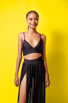 A fashionable woman posing confidently in a black outfit against a vibrant yellow backdrop.