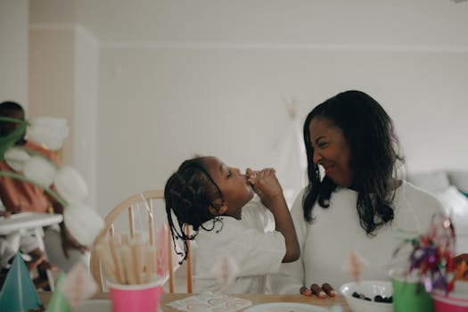 A mother and daughter share a joyful moment during a birthday celebration with festive decorations.