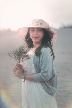 日落时分，一位戴帽子的女人在海滩上手持树枝微笑的肖像