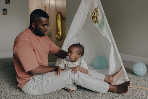 
A Man Holding His Child while Sitting on the Floor