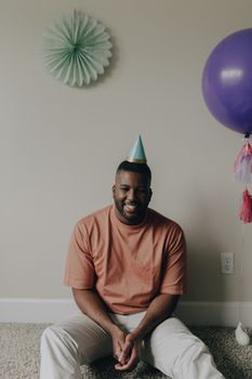 A smiling man celebrating a birthday indoors with festive decorations and balloons.
