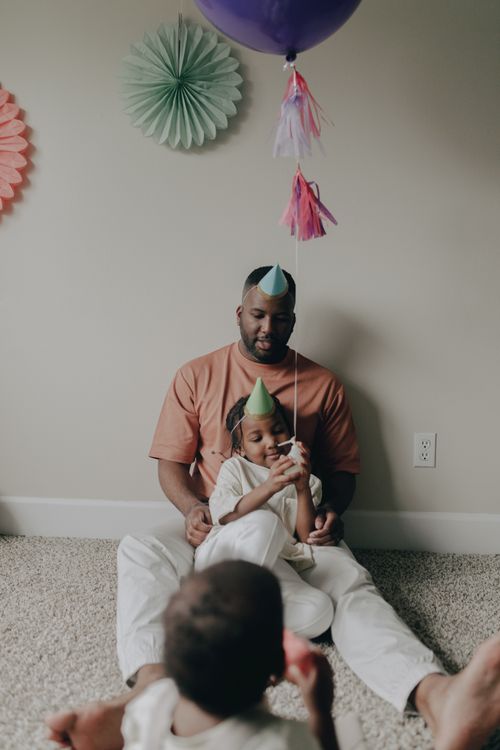 Free African father celebrates a child's birthday indoors with party hats and decorations. Stock Photo