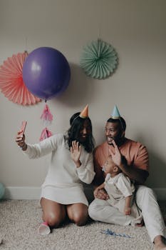 A joyful family celebrating a birthday with balloons and party hats indoors.