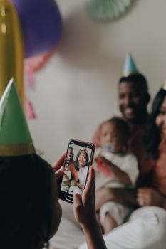 A family captures a birthday moment on smartphone, featuring smiles and party hats.