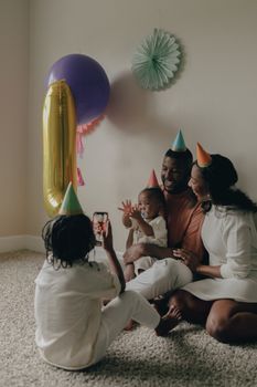 Family celebrating a baby's first birthday with party hats and decorations. Captured indoors.